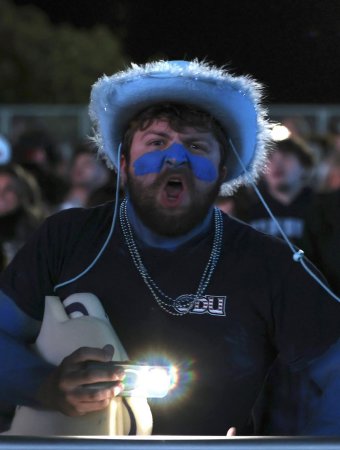 Adyn shows his school spirit at an evening football game. He wears a feathered blue hat, blue face paint, ODU shirt and silver beads as he cheers, facing the camera directly.