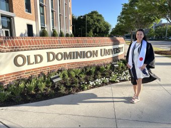 Mana Roberts standing in front of Old Dominion University in commencement gown.