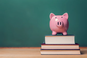 Piggy bank on top of books with chalkboard, cost of educatio