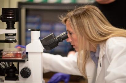 Woman in lab coat looking into microscope