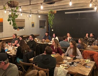 Residency students sit at tables in dimly lit restaurant dining room.