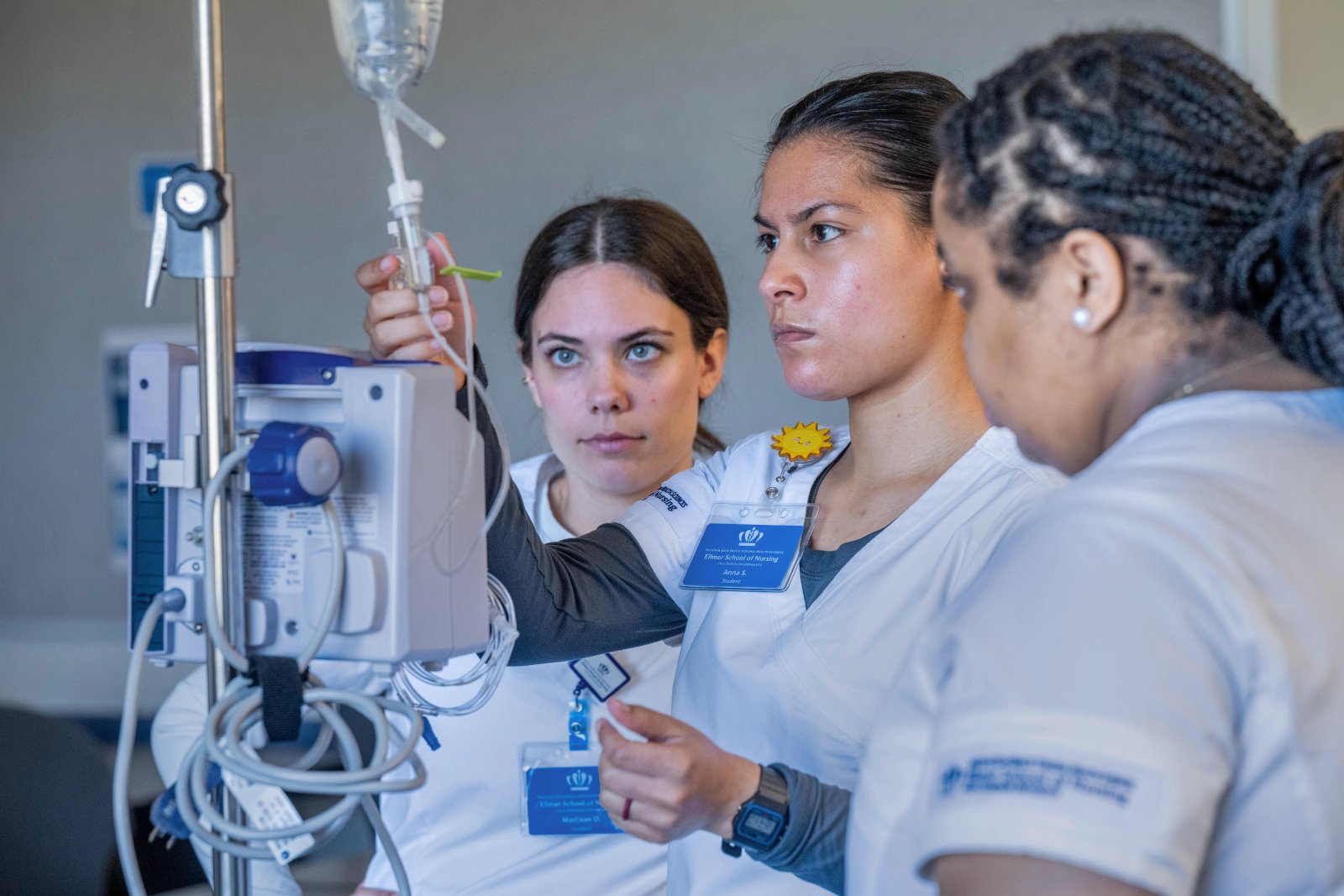 Three nursing students practice with IV machine.