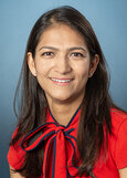 Dr. Patel has long, straight dark hair, is wearing a bright  red shirt